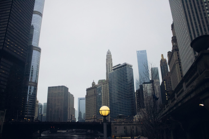 View of the Chicago Riverwalk in December, featuring a glowing yellow lamp contrasted against icy blue tones. Skyscrapers rise on both sides of the misty river, with a bridge ahead adding depth to the urban winter scene.