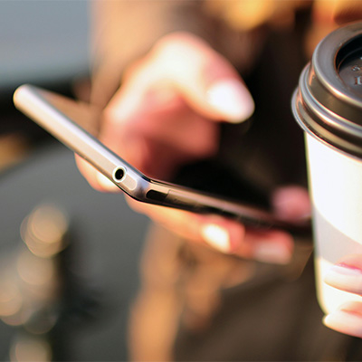 Person holding a smartphone and a coffee, representing custom art commissions.